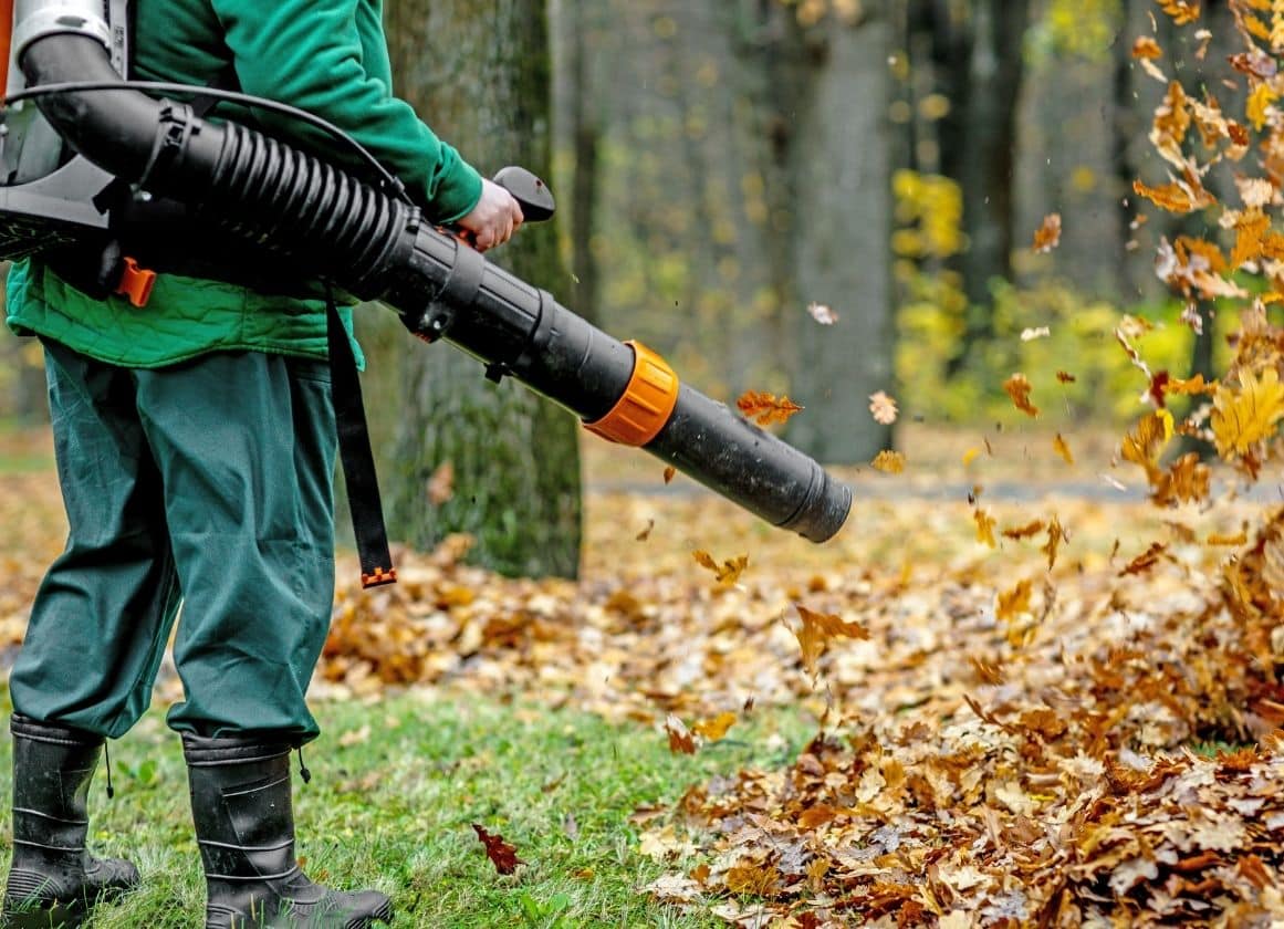 Paysagiste utilisant un souffleur de feuilles pour nettoyer et entretenir un espace vert en période automnale.