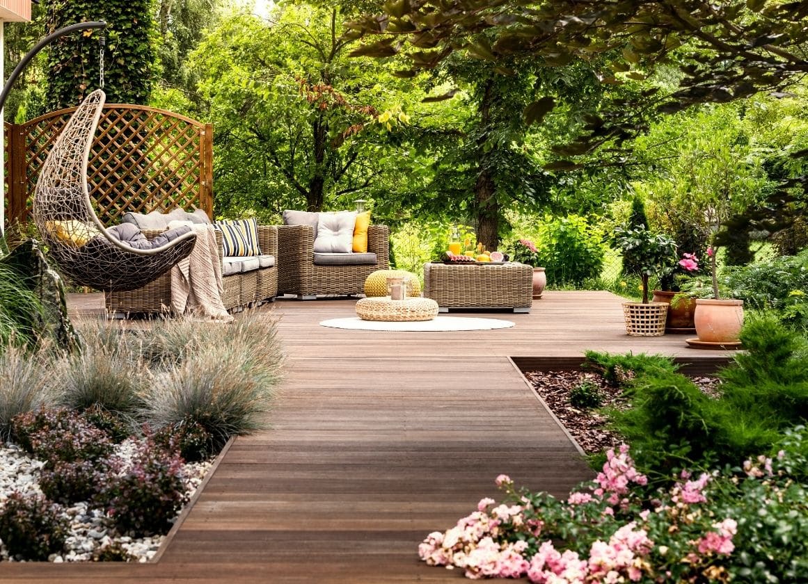 Terrasse en bois aménagée avec mobilier de détente, massifs fleuris et végétation paysagère dans un jardin soigné.