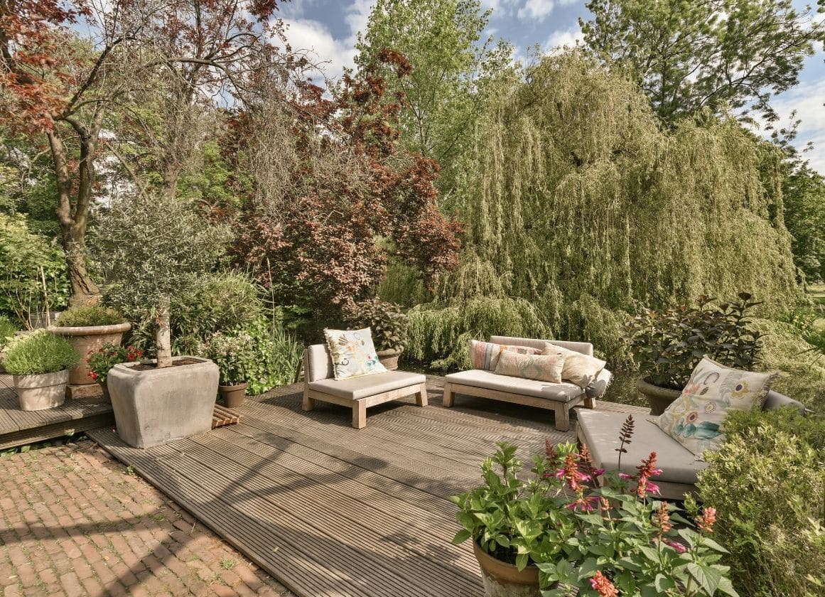 Terrasse en bois aménagée avec mobilier de détente, végétaux ornementaux et jardin paysager arboré.
